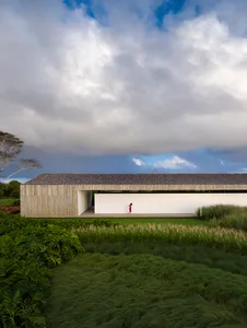 A modern house with green packgrass in the foreground and a cloudy sky above.