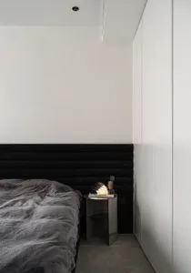 A modern minimalist bedroom featuring a black upholstered bed and a metallic bedside table with a modern lamp.