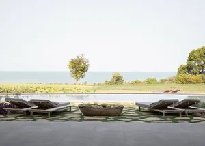 A minimalist residential patio featuring wooden furniture and a wooden bowl filled with green coconuts, overlooking a serene