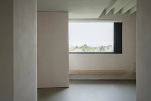 極簡房間擁有混凝土地板與牆面，設有大型窗戶可俯瞰住宅區。