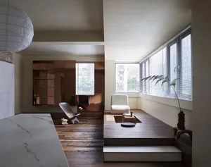 A modern living room featuring a wooden platform, minimalist furniture, and large windows with blinds.