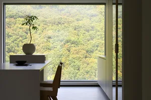 A minimalist sitting area with glass window frame overlooking a lush forest.