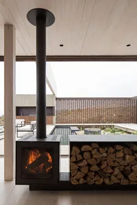 Modern industrial outdoor living space with a concrete fireplace, metal chimney, and wooden accents surrounded by a metal mes