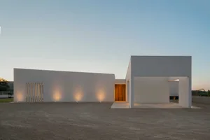 A minimalist home with white walls and a concrete patio at dusk.