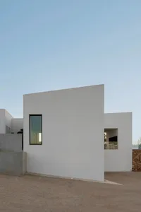 A minimalist modern house with white walls and geometric shapes, featuring a small rectangular window.