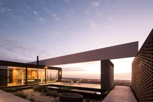 Modern minimalist residential outdoor space featuring concrete and glass materials with a view of a sunset sky.