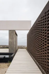 A modern building exterior featuring a concrete structure with a wooden walkway and a perforated wooden wall.
