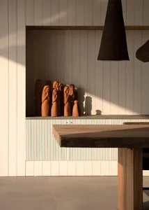 Modern dining room featuring wooden table and concrete floor with wooden carvings in the background.