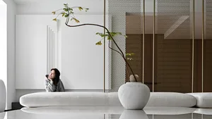 A minimalist living room with white furniture and a glass wall.