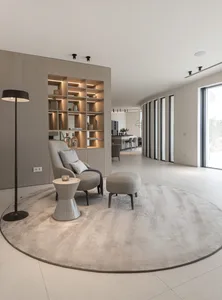 Modern minimalist living room with a contemporary design featuring a plush chair, an ottoman, a standing lamp, built-in shelv