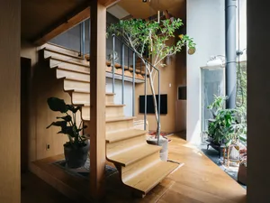 Modern staircase made of wooden steps and railing with a potted plant beside it, on a hardwood floor.