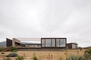 A modern glass house with large windows and concrete foundation.