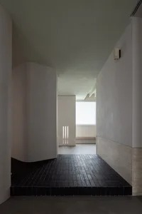 A modern, minimalistic corridor with a concrete floor, white walls, and a window with blinds.