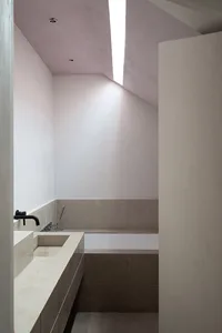 A modern minimalist bathroom with concrete walls and floor, featuring a sleek white bathtub and a built-in sink.