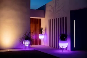 Three illuminated plastic planters with purple lighting, placed in front of a modern minimalist building entrance.