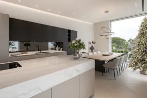 Modern, minimalist residential kitchen featuring marble countertops and a large dining area with a white Christmas tree and o