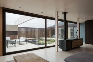 A modern living area with timber flooring, minimalistic design, and natural light, featuring seating and a fireplace.