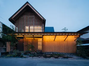 A modern residential house made of wood with a warm interior light and a garden in front.