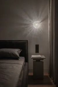 A modern bedroom featuring dark bedding and a wall-mounted light fixture casting a warm glow.