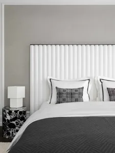 A minimalist bedroom featuring a white fabric headboard and a marble side table.