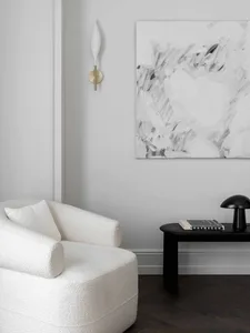 Minimalist living room featuring a textured plush armchair, abstract black and white artwork, black side table, and sleek bla