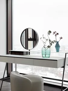 Modern, minimalist office workspace featuring a sleek white desk and round mirror in front of a large window with a snowy cit
