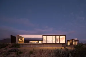 A modern residential house featuring large glass windows, concrete exterior, and wooden accents at dusk.