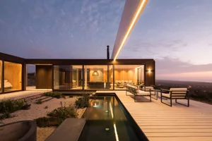 Modern residential house with a wooden exterior, large windows, and lighting features during twilight.