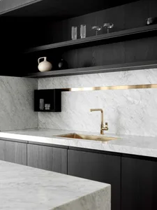 A modern kitchen featuring a marble countertop and backsplash, with black cabinetry and a gold faucet