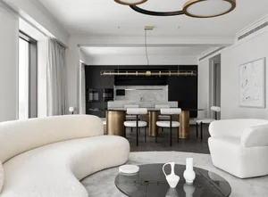 Modern living room featuring a white circular sofa, a black coffee table with white vases, and a kitchen area with black cabi