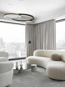 A modern white living room featuring a circular light fixture and curved sofa.