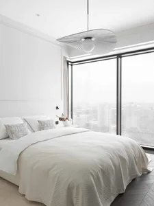 A minimalist bedroom featuring a white textured cotton blanket on a bed with a panoramic window showing a cityscape.
