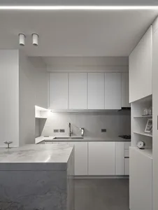 Modern, minimalist kitchen featuring marble countertops, concrete backsplash, and white cabinetry with sleek, modern design.