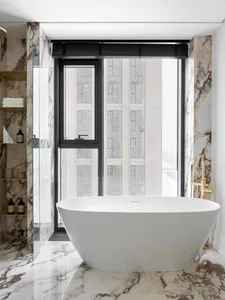 Modern bathroom with a freestanding bathtub placed in front of a large window with a city view, featuring marble walls and fl