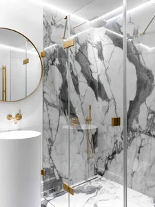 A modern bathroom featuring marble walls and floor, with a glass shower enclosure and brass fixtures.