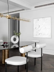 A modern dining room featuring white leather chairs, metallic accents, and a geometric light fixture.