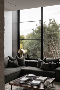 Modern gray living room with a comfortable fabric sofa, large windows with a view of greenery, and a metallic table lamp.