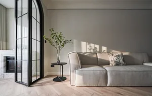 Modern minimalist living room featuring a light gray fabric couch with a small black side table holding a vase of greenery.
