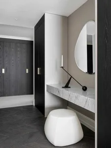 A modern vanity with marble countertop and white leather ottoman, featuring a minimalist design with a rounded mirror and bla