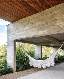 A modern, minimalist exterior made from concrete materials with a covered patio area and a white hammock.