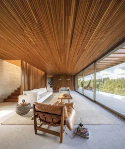 A modern living room featuring a wood-paneled ceiling and floor-to-ceiling glass windows, incorporating a mix of contemporary