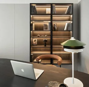 A modern minimalist office setup featuring a dark wooden desk, a green and black lamp, and a black bookshelf filled with book