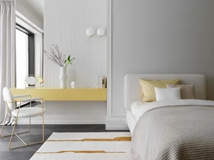 A modern bedroom featuring a textured wallpaper wall, a white bed with yellow pillows, a yellow desk with a vase and books, a