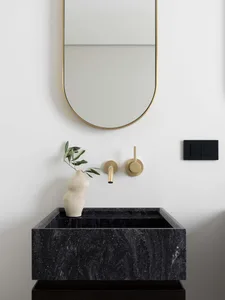 Modern bathroom with black marble sink, brass fixtures, and a minimalist design.