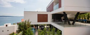 A modern residential exterior featuring glass walls and a swimming pool overlooking the sea.