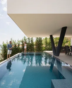 A modern swimming pool with concrete walls and a covered patio area.