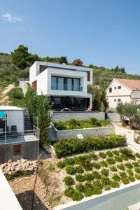 Modern villa with white exterior walls, glass windows, and stone accents, featuring a landscaped garden and outdoor seating a