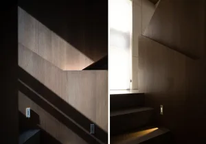 Minimalist interior design showcasing a wooden staircase with a light fixture and sunlight streaming through a window.