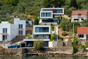A modern residential house with glass, concrete, and stone exteriors located near a body of water.