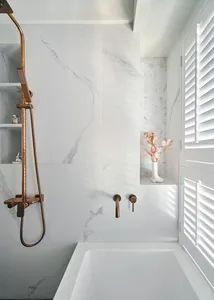 Modern bathroom with a white bathtub, copper faucets, and a marble wall.